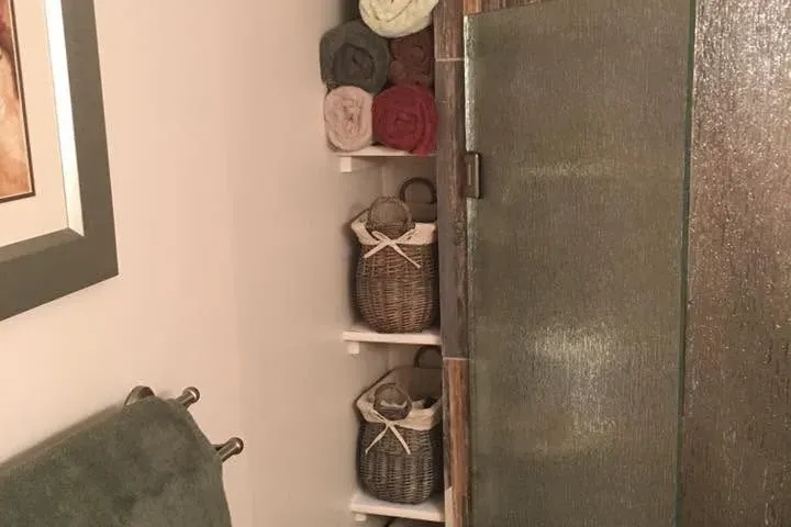 Glass shower with wood-look tile beside corner towel shelving, C&A Roofing & Construction
