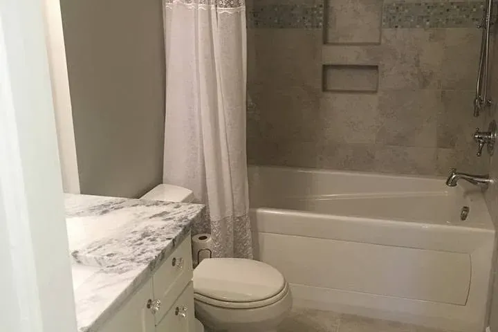 Small bathroom with tub, toilet, marble vanity, shower curtain, C&A Roofing & Construction