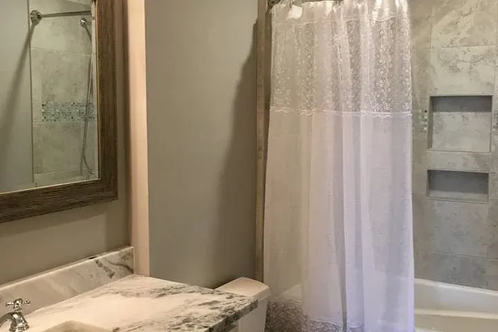 Bathroom with marble vanity, mirror, toilet, curtain tub, C&A Roofing & Construction