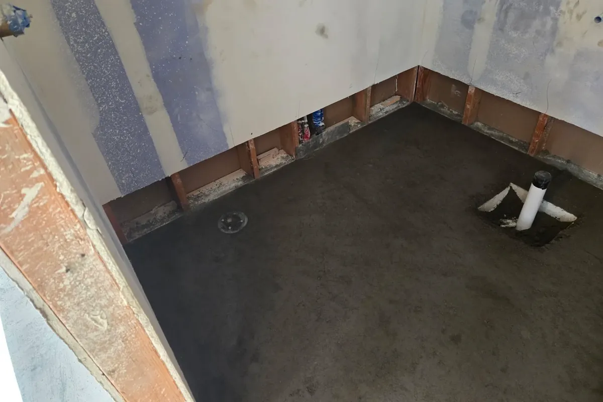 Gutted bathroom floor with shower pan prep, bare walls, C&A Roofing & Construction