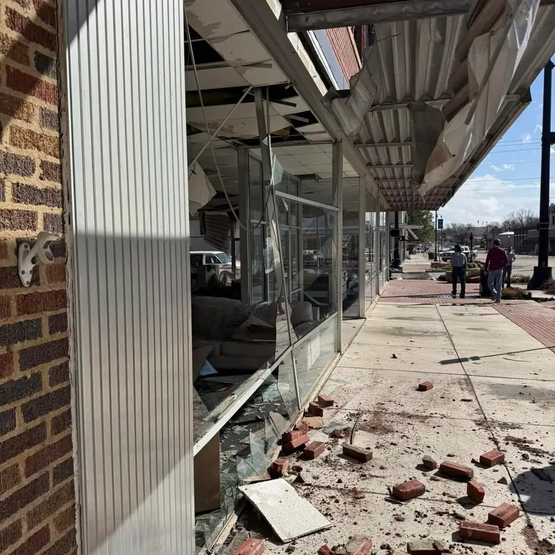 Storefront with shattered windows and brick rubble on sidewalk, C&A Roofing & Construction