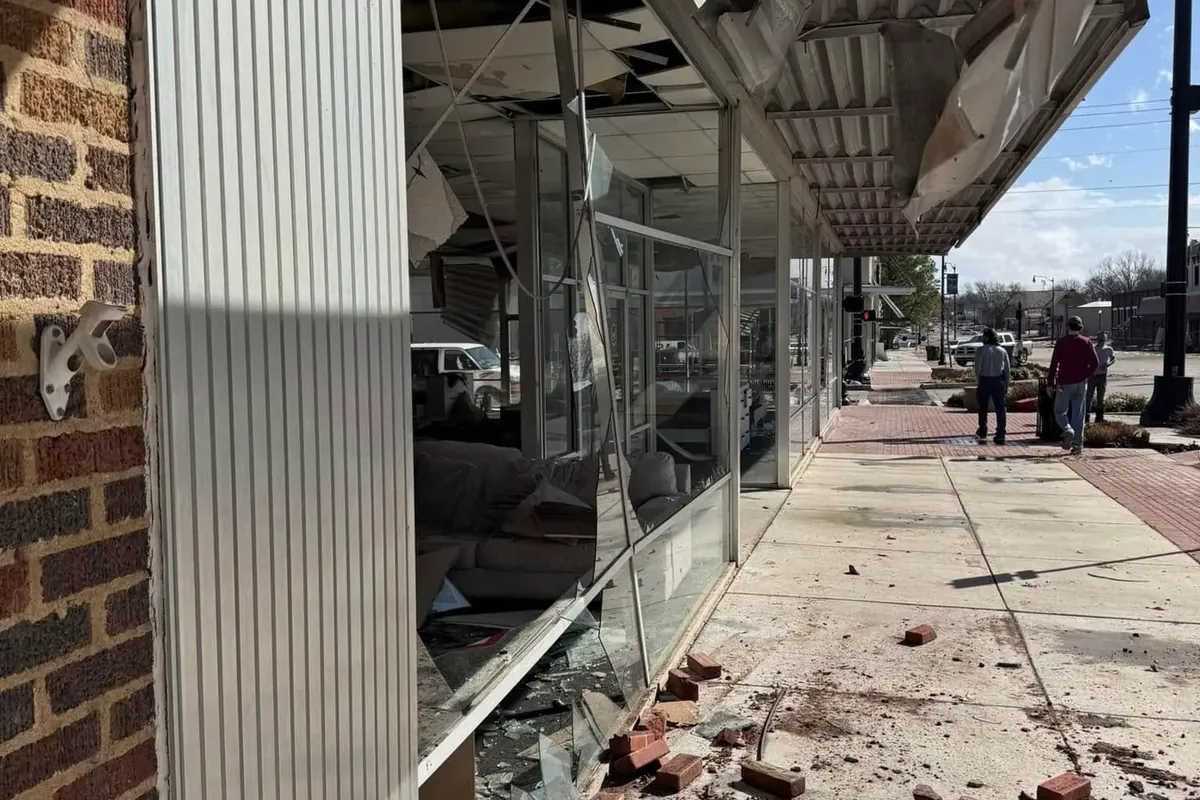 Storefront with shattered windows and brick rubble on sidewalk, C&A Roofing & Construction