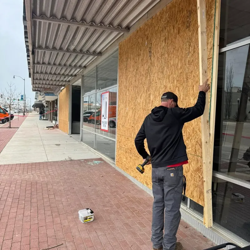 Worker boarding up damaged storefront with plywood, C&A Roofing & Construction