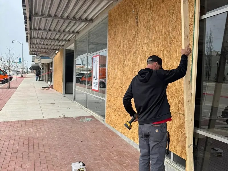 Worker boarding up damaged storefront with plywood, C&A Roofing & Construction