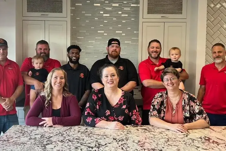 Team group photo seated around granite island, C&A Roofing & Construction