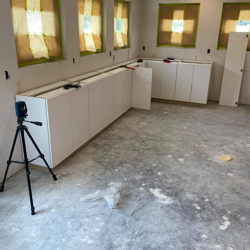 Base cabinets being installed in empty kitchen on bare slab, C&A Roofing & Construction