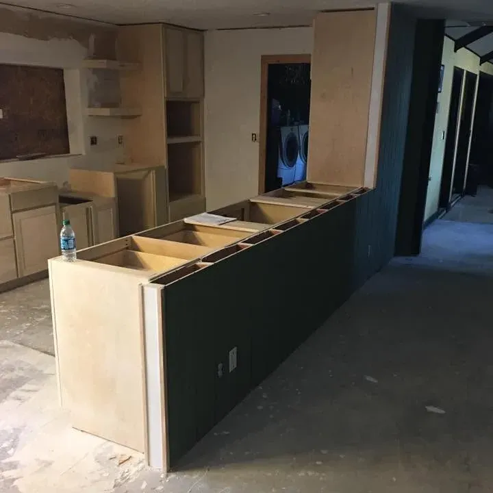 Unfinished cabinets with dark-painted peninsula on bare slab, C&A Roofing & Construction
