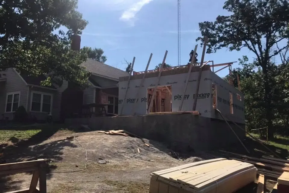 Addition framing on stone house against bright sky, C&A Roofing & Construction