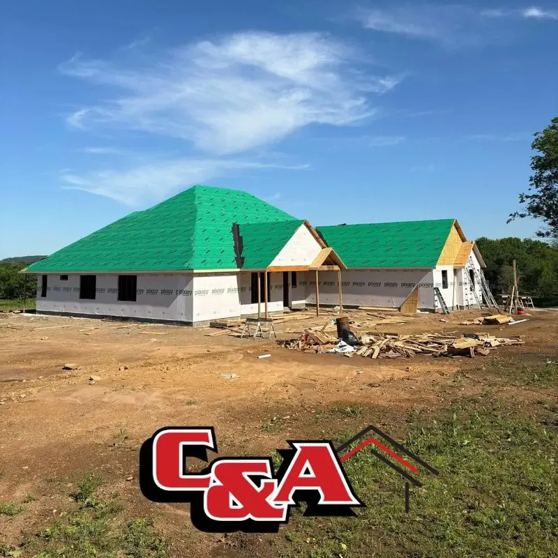 Framed house with green roof underlayment on dirt lot, C&A Roofing & Construction