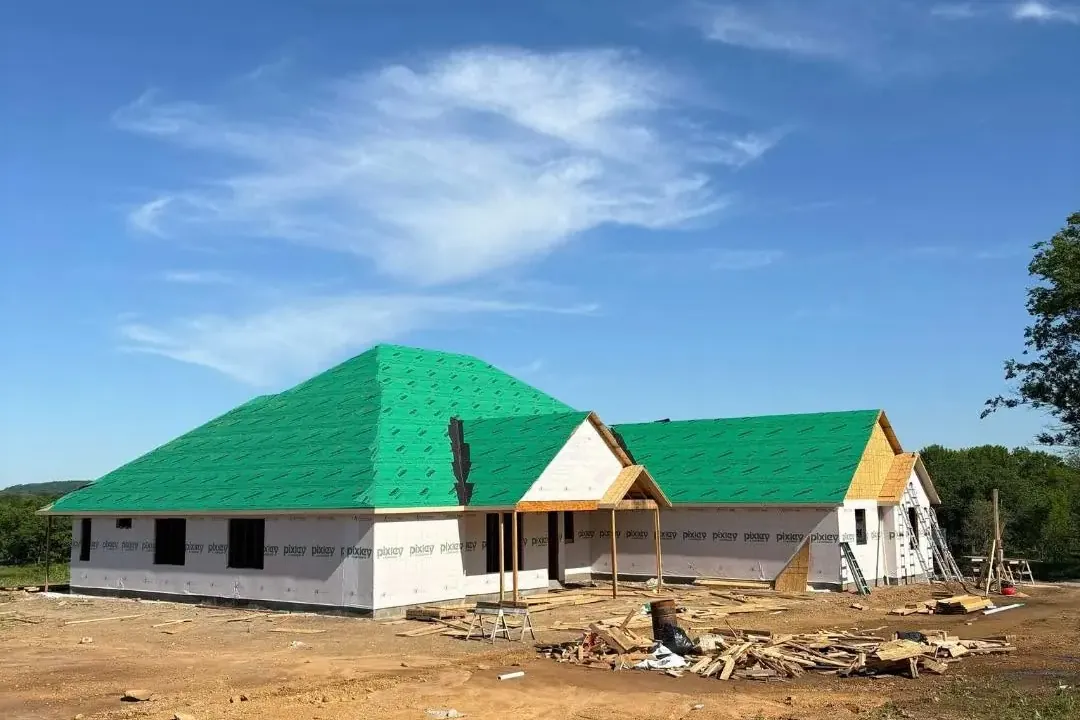Framed house with green roof underlayment on dirt lot, C&A Roofing & Construction