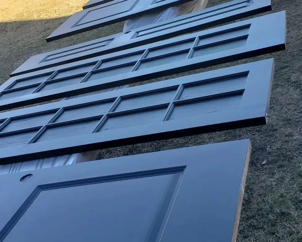 Row of freshly painted navy panel doors drying on grass, C&A Roofing & Construction