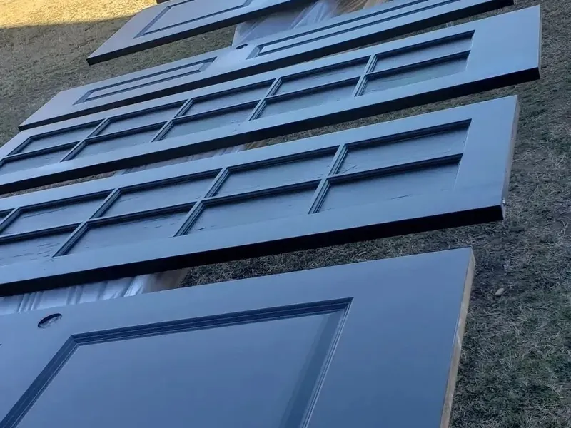 Row of freshly painted navy panel doors drying on grass, C&A Roofing & Construction