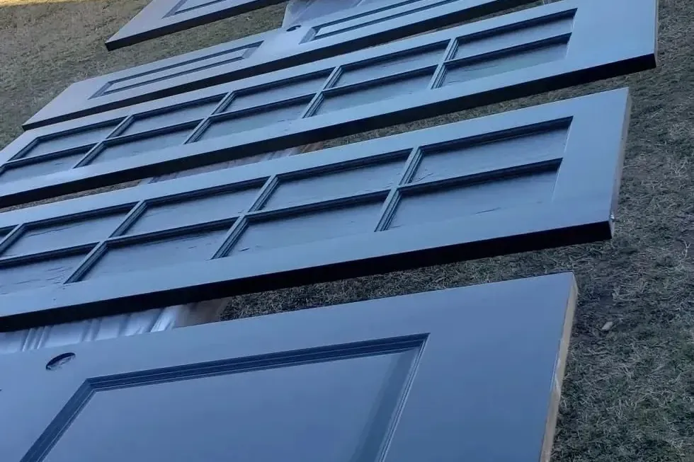 Row of freshly painted navy panel doors drying on grass, C&A Roofing & Construction