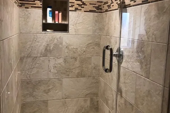 Tiled walk-in shower with accent band, niche and glass door, C&A Roofing & Construction