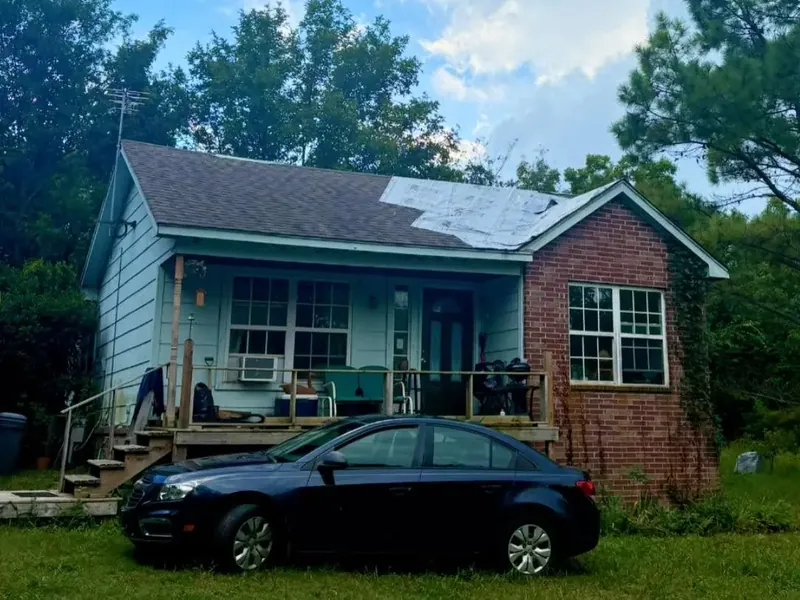 Blue house with partially tarped/damaged roof, car in front, C&A Roofing & Construction