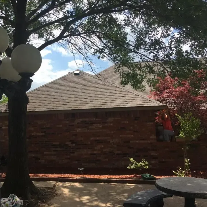 Brick house with brown shingle roof behind lamp post and tree, C&A Roofing & Construction