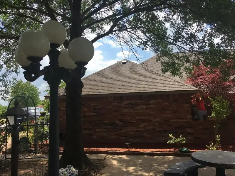 Brick house with brown shingle roof behind lamp post and tree, C&A Roofing & Construction