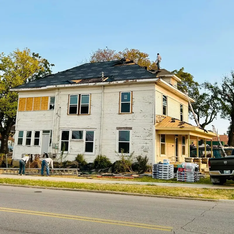 Old two-story house with crew re-roofing, materials stacked, C&A Roofing & Construction