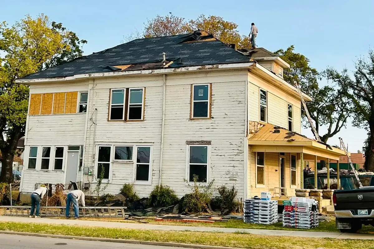 Old two-story house with crew re-roofing, materials stacked, C&A Roofing & Construction