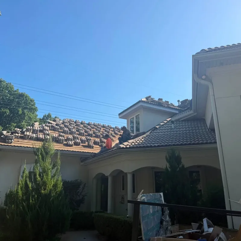 Large stucco home with tile roof being installed, materials stacked, C&A Roofing & Construction
