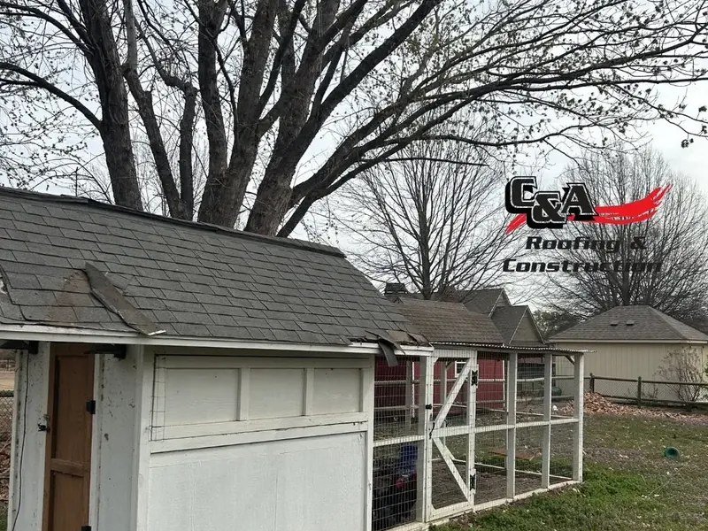 White shed with damaged shingle roof and fenced run, C&A Roofing & Construction