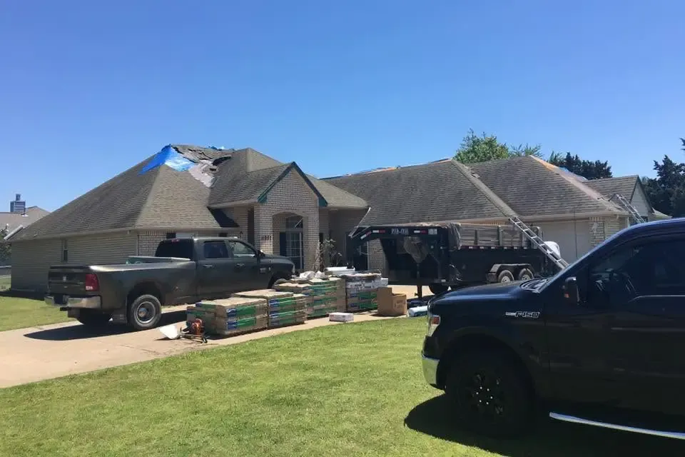 Brick house roof with tarp, materials on drive, trucks parked, C&A Roofing & Construction