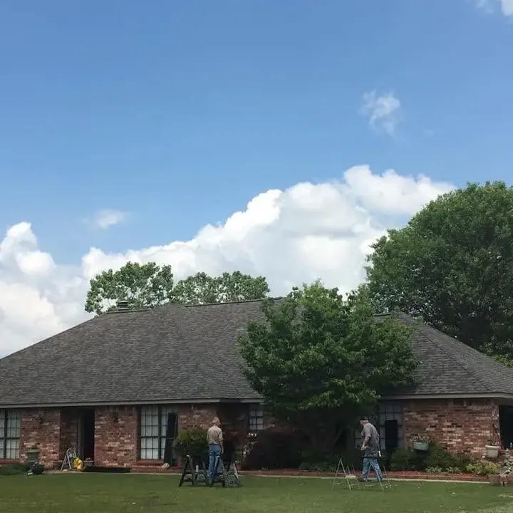 Brick ranch with dark shingle roof, two men working on porch, C&A Roofing & Construction
