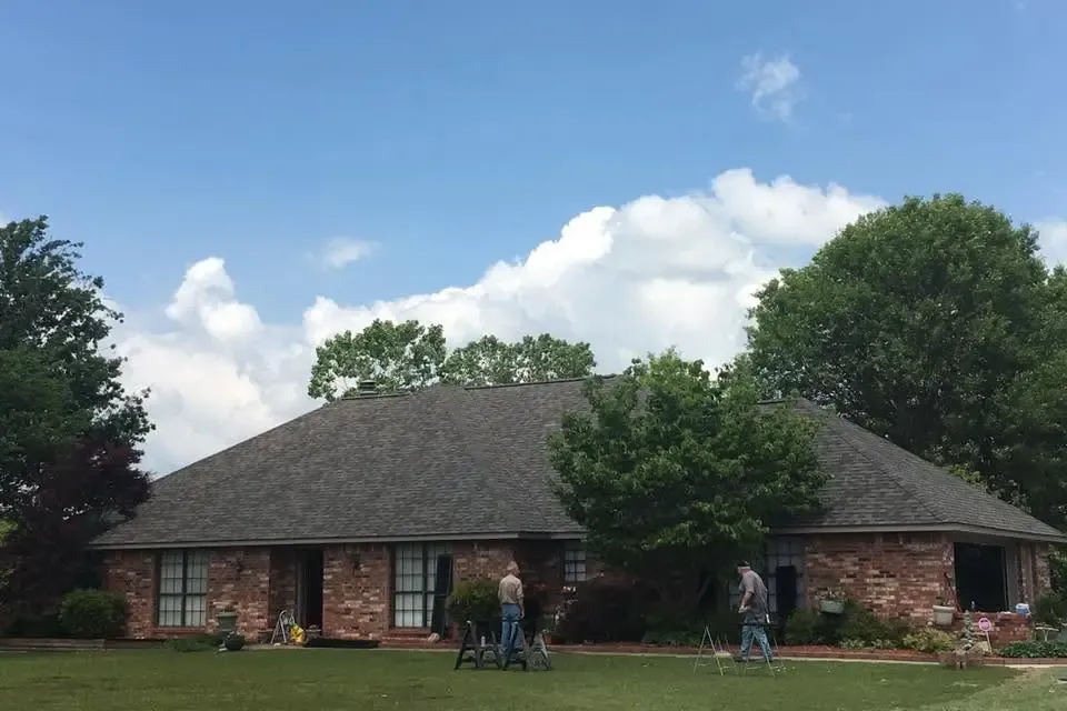Brick ranch with dark shingle roof, two men working on porch, C&A Roofing & Construction