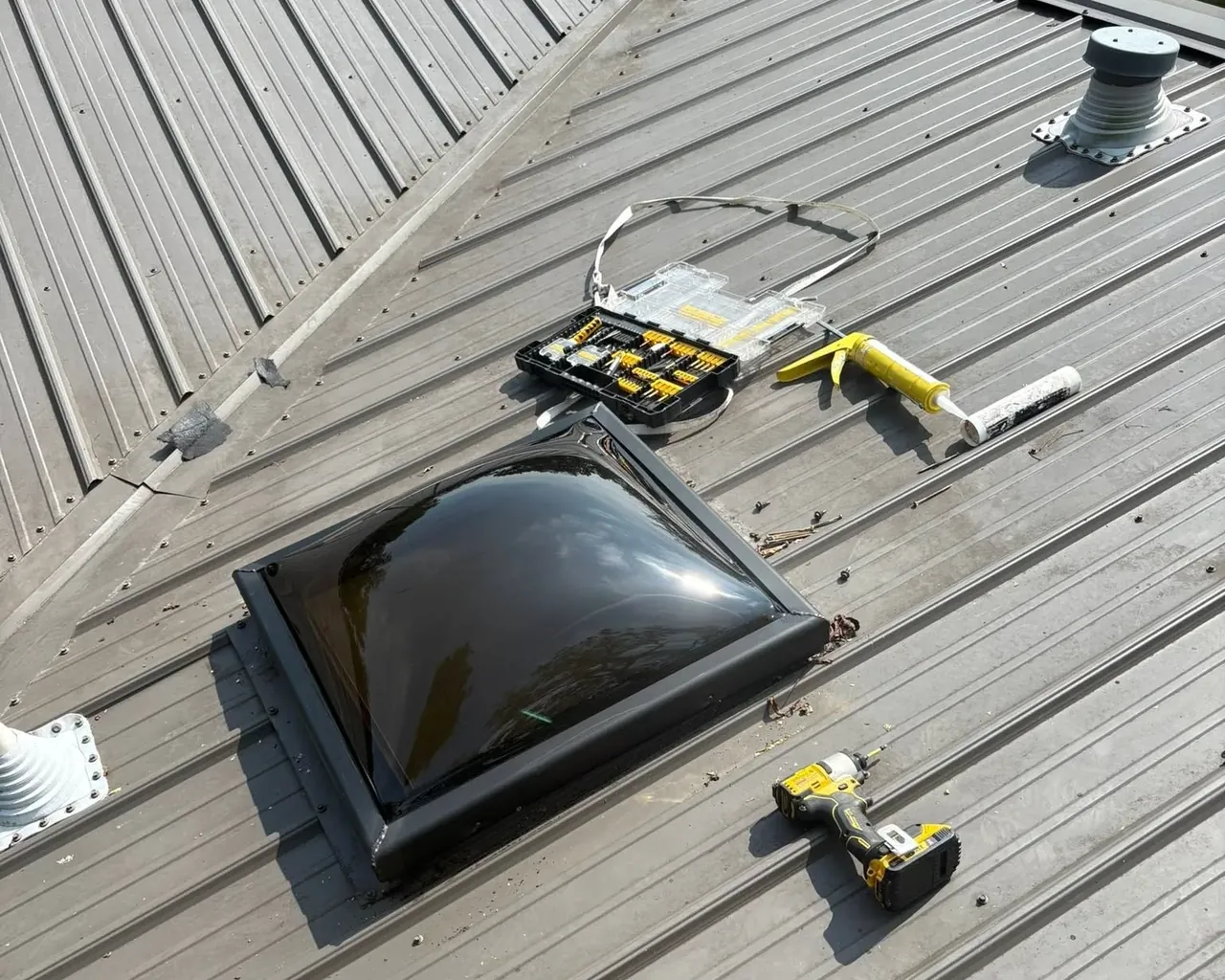 Skylight dome being installed on tan metal roof with tools, C&A Roofing & Construction
