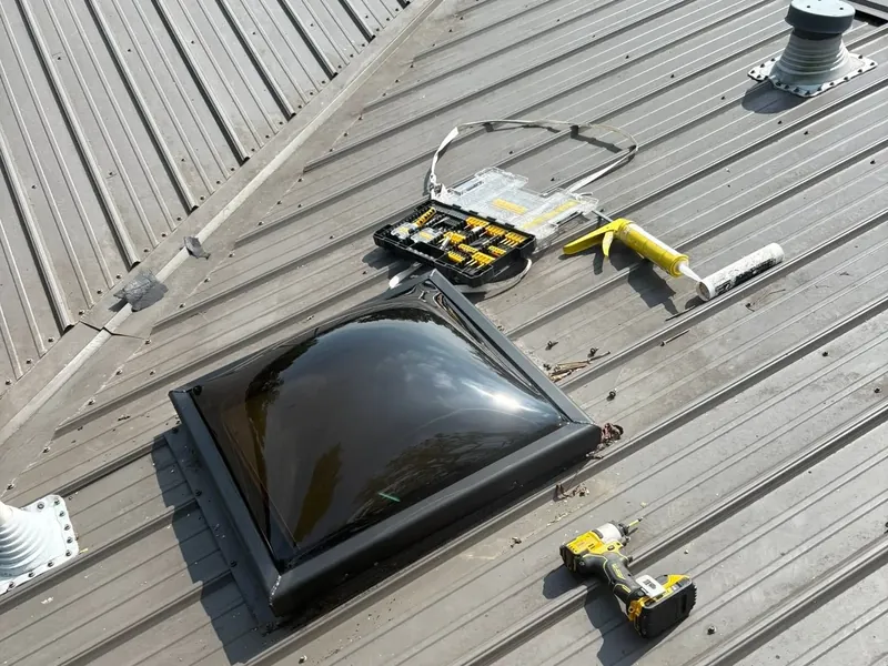 Skylight dome being installed on tan metal roof with tools, C&A Roofing & Construction