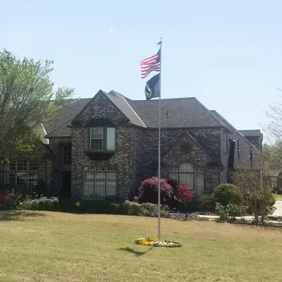 Distant two-story brick house with dark roof and flagpole, C&A Roofing & Construction