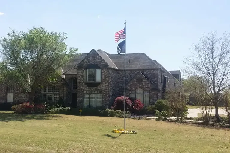 Distant two-story brick house with dark roof and flagpole, C&A Roofing & Construction