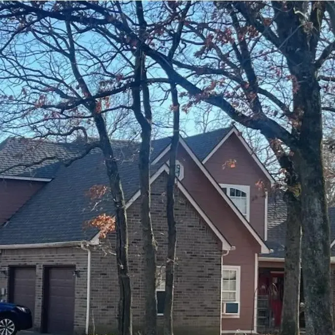 Two-story brick house with dark shingle roof among trees, C&A Roofing & Construction