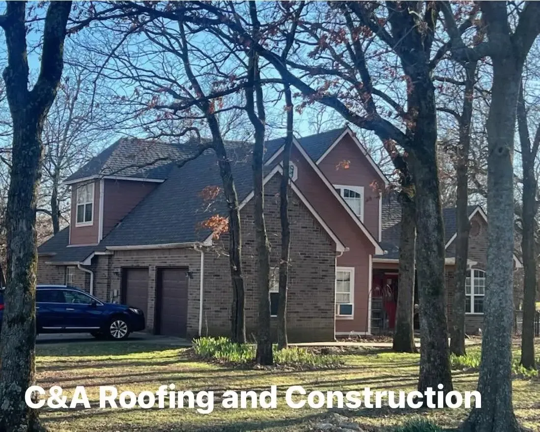 Two-story brick house with dark shingle roof among trees, C&A Roofing & Construction