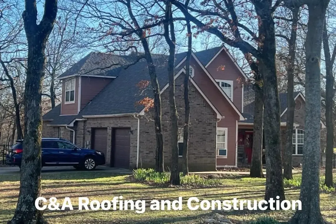 Two-story brick house with dark shingle roof among trees, C&A Roofing & Construction