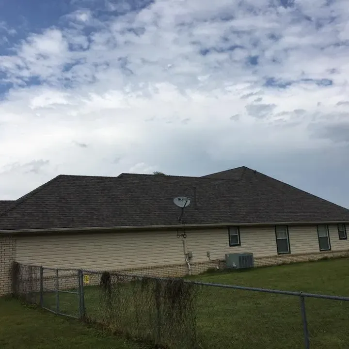 Tan ranch house with dark shingle roof behind fence, C&A Roofing & Construction