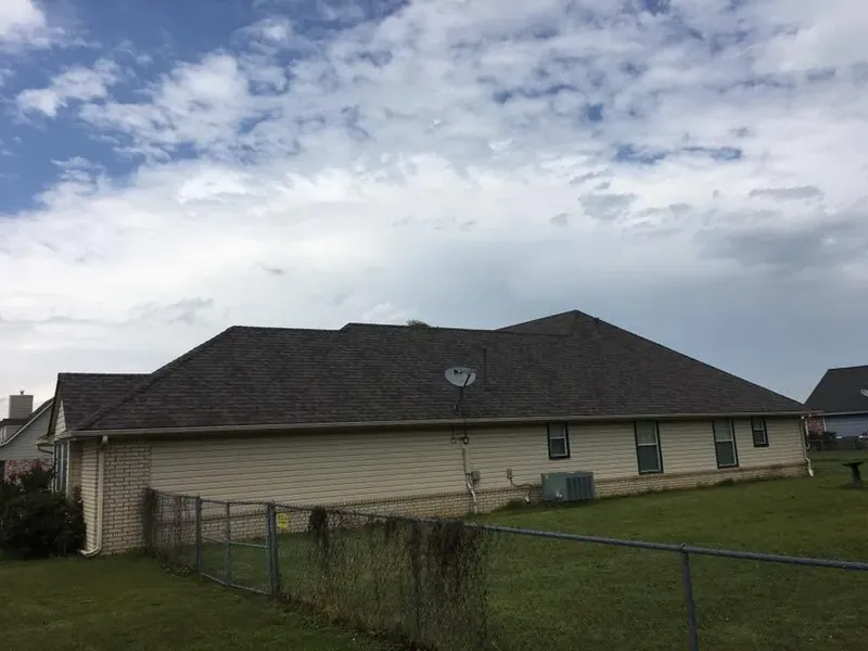 Tan ranch house with dark shingle roof behind fence, C&A Roofing & Construction