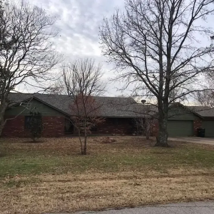 Brick ranch with shingle roof behind bare trees, C&A Roofing & Construction