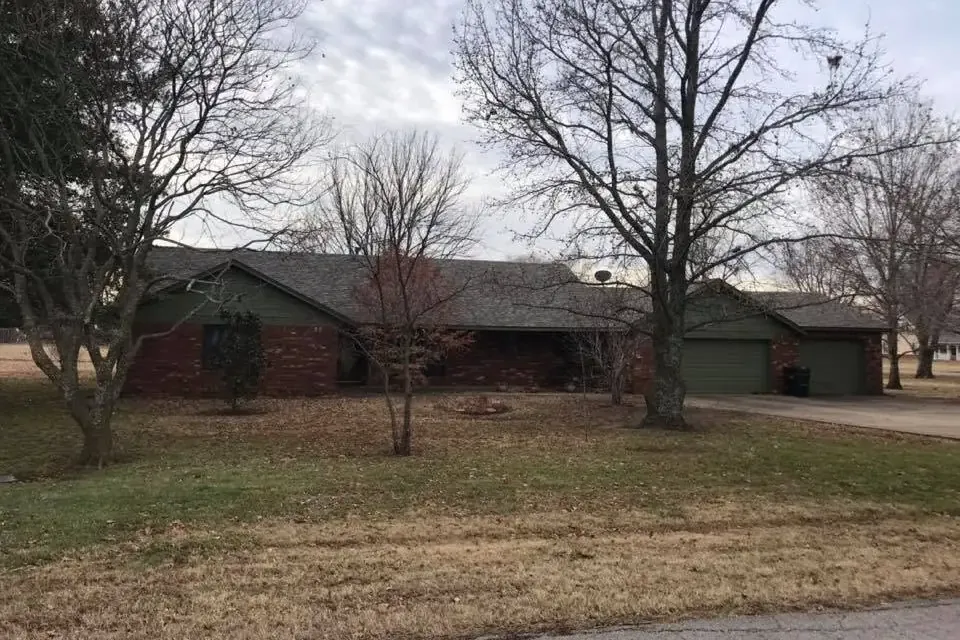 Brick ranch with shingle roof behind bare trees, C&A Roofing & Construction
