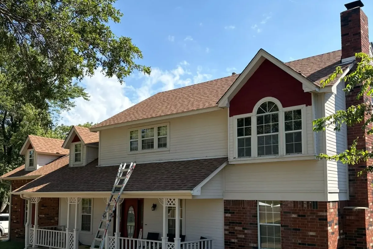 Two-story house roof work in progress, ladder at porch, C&A Roofing & Construction