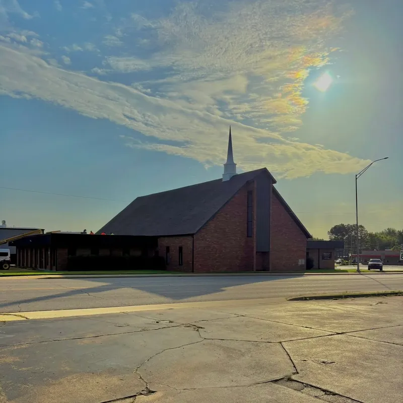 Backlit brick church with steeple, crew tiny on flat roof section, C&A Roofing & Construction