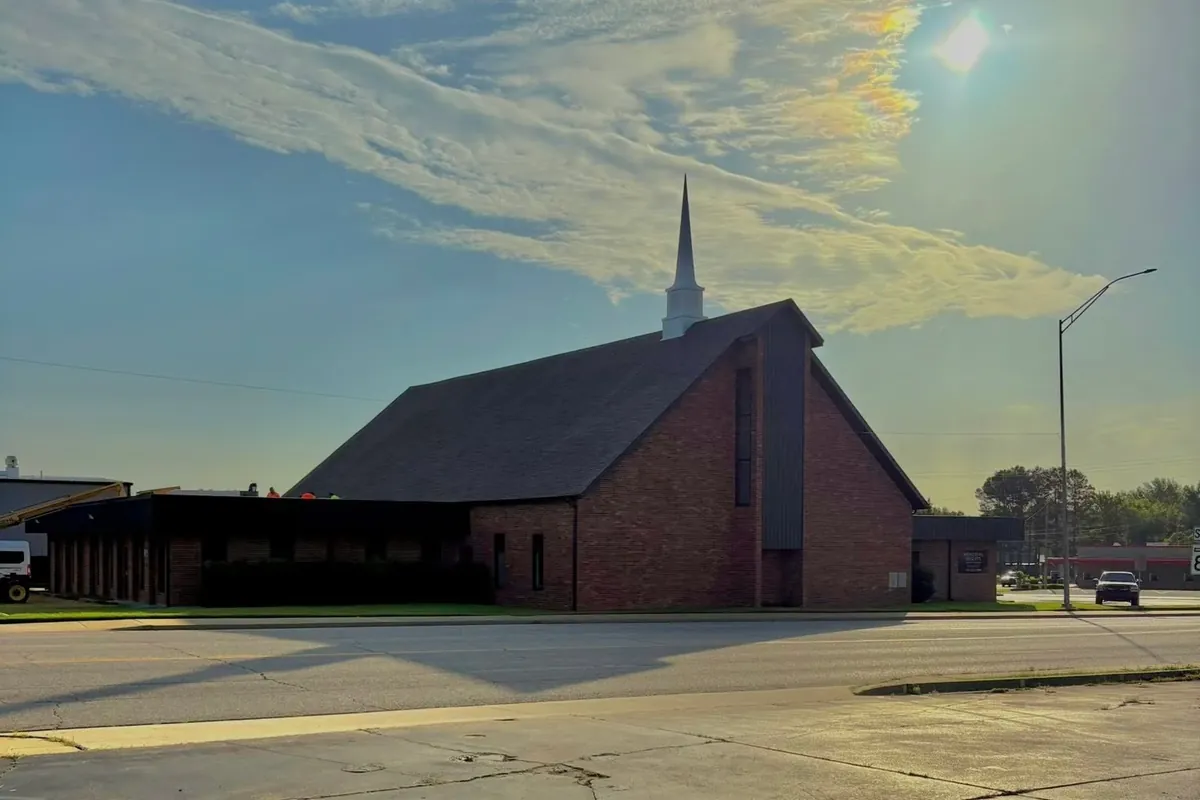 Backlit brick church with steeple, crew tiny on flat roof section, C&A Roofing & Construction