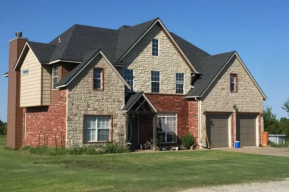 Two-story stone and brick house with new dark shingle roof, C&A Roofing & Construction