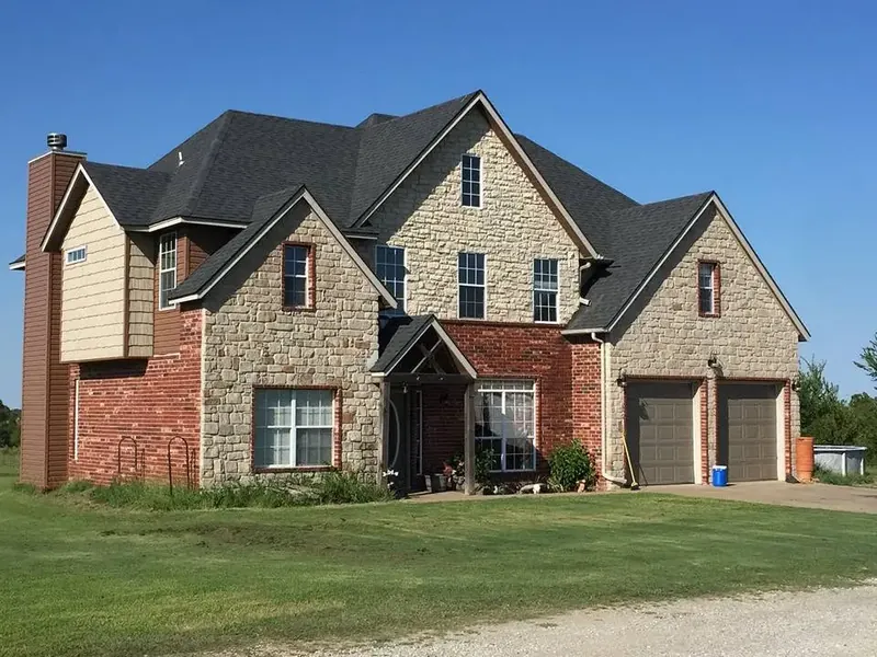 Two-story stone and brick house with new dark shingle roof, C&A Roofing & Construction